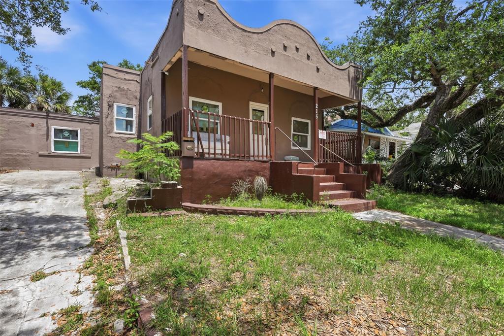 A brown, single-story house with a front porch, a concrete driveway, and overgrown landscaping — 215 S OLEANDER AVENUE, DAYTONA BEACH, FL