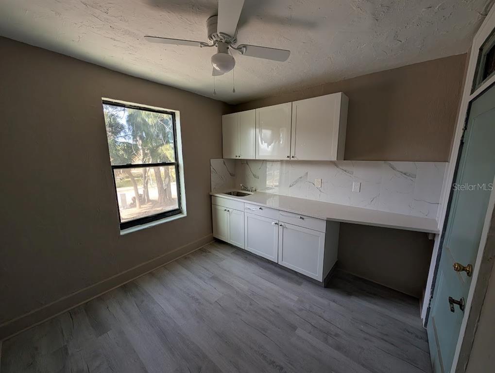 A small kitchen features white cabinets, a marble-look backsplash, light wood flooring, and a ceiling fan — 401 COLONIA LANE E UNIT 8, NOKOMIS, FL