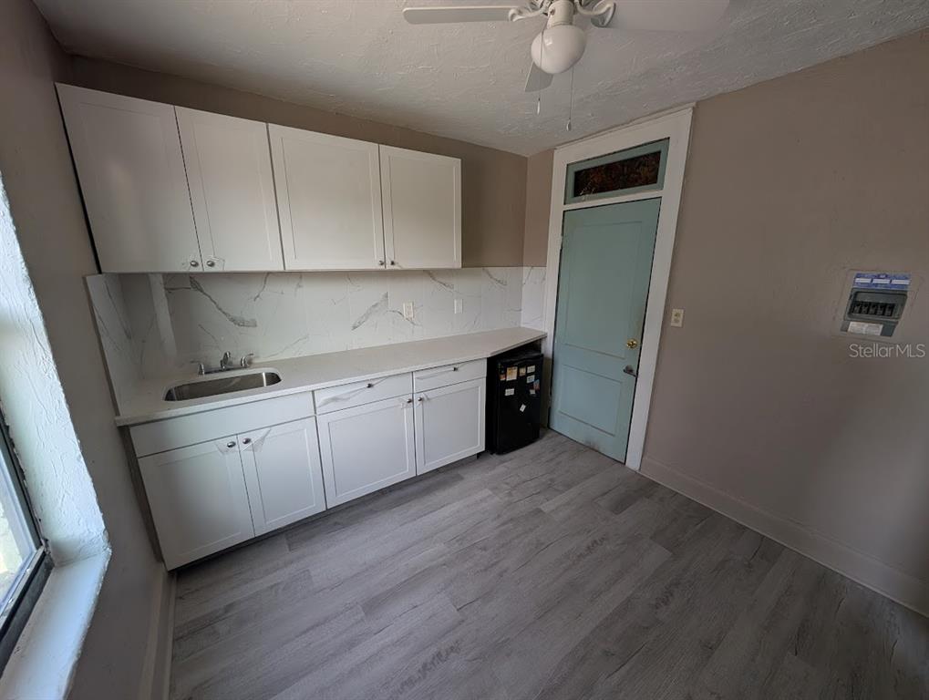 A kitchen features white cabinets, a marble-look backsplash, a small sink, and light wood flooring — 401 COLONIA LANE E UNIT 8, NOKOMIS, FL