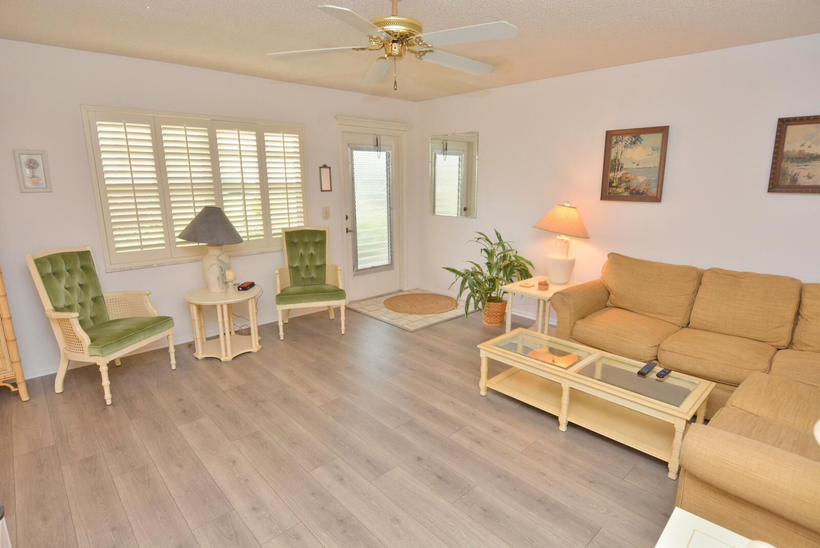 A living room featuring light wood-look flooring, a beige sectional sofa, and two green chairs — 1225 NW 21st Street # 3506, Stuart FL 34994, STUART, FL