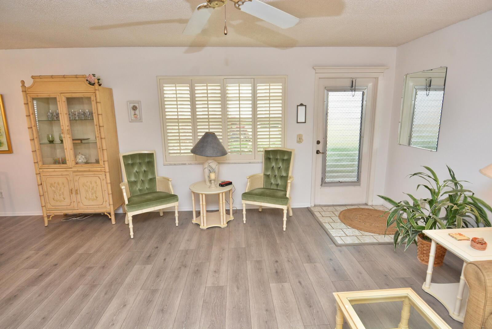 A living room features wood-look flooring, two green velvet chairs, a hutch, and a front door — 1225 NW 21st Street # 3506, Stuart FL 34994, STUART, FL