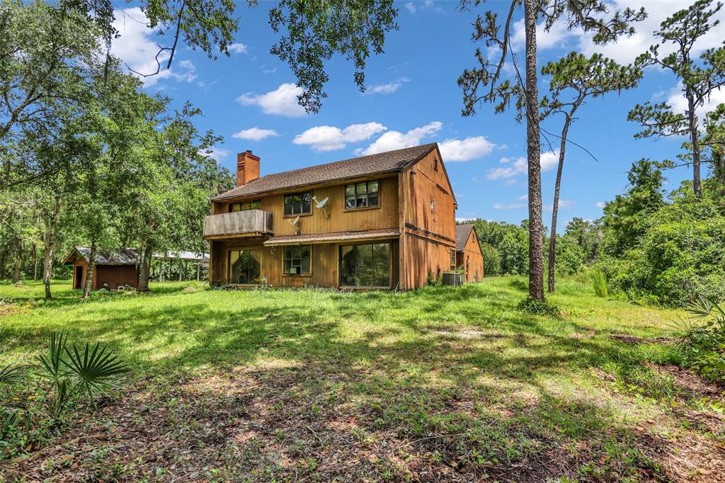 A two-story wooden house with a balcony and a detached shed sits on a grassy lot — 24003 SISLER AVENUE, CHRISTMAS, FL