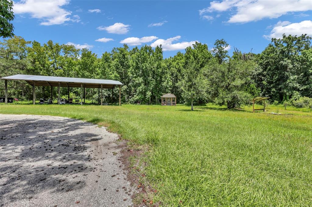 A gravel driveway leads to a large metal carport and a small shed in a field — 24003 SISLER AVENUE, CHRISTMAS, FL