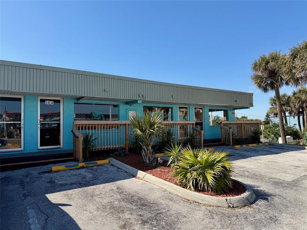 A turquoise commercial building features a wooden deck, parking spaces, and several palm trees — 3400 S ATLANTIC AVENUE UNIT 3400 & 3404, DAYTONA BEACH, FL