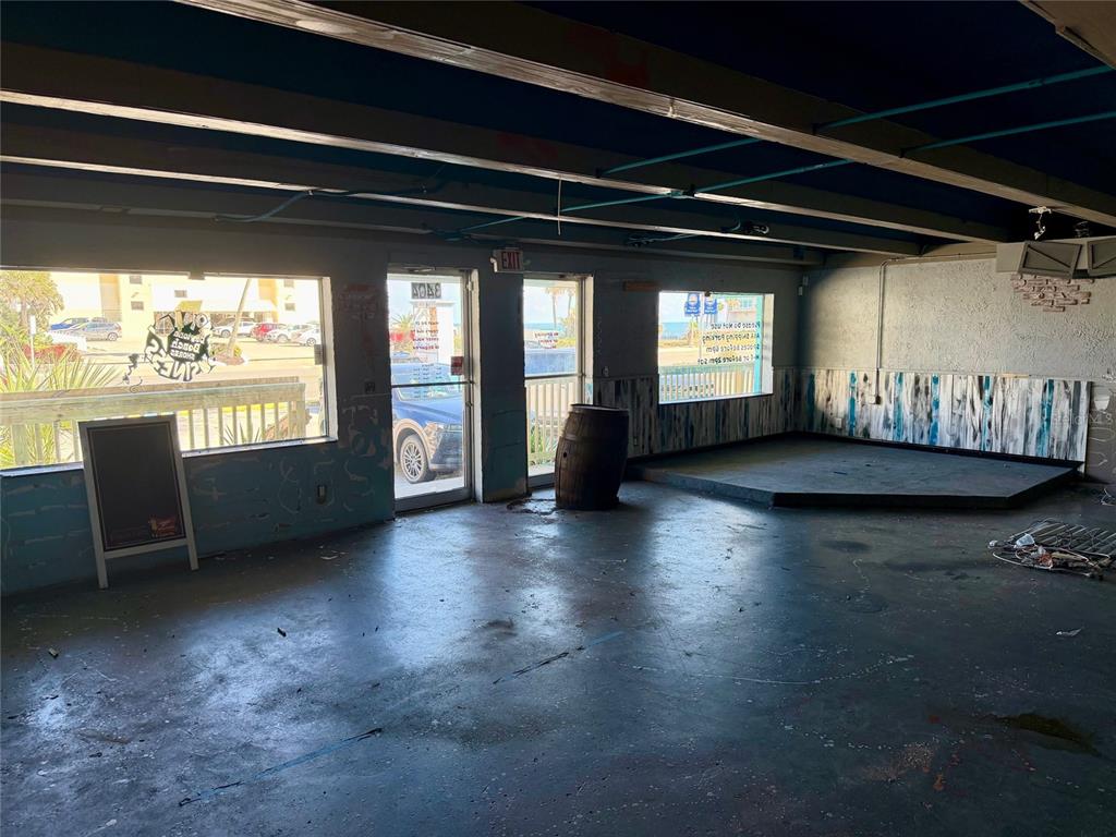 An interior view of a vacant commercial space with concrete floors, windows, and a small stage — 3400 S ATLANTIC AVENUE UNIT 3400 & 3404, DAYTONA BEACH, FL