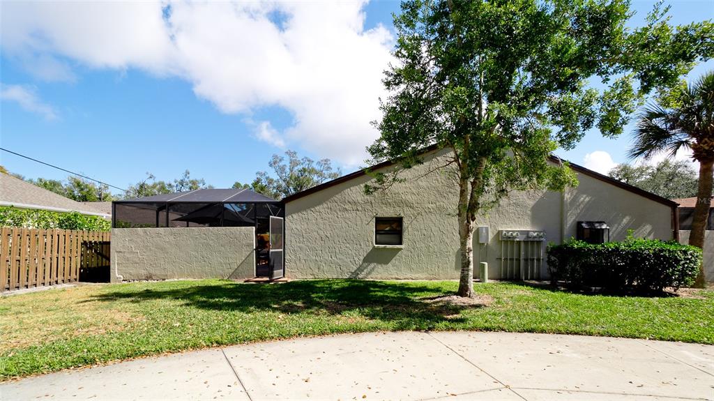 The exterior of a house features a stucco wall, a screened-in patio, and a tree — 4527 PARK LAKE TERRACE N, BRADENTON, FL