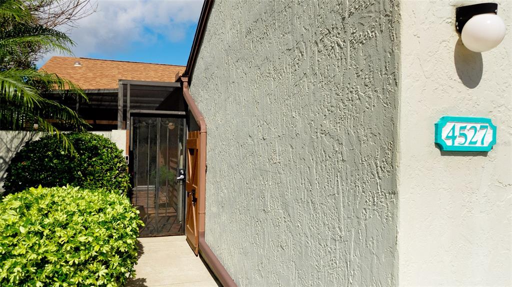 A textured exterior wall features a house number plaque and a light fixture near an entrance — 4527 PARK LAKE TERRACE N, BRADENTON, FL