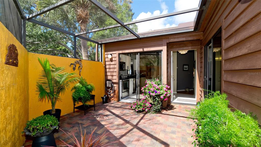 A screened-in patio features brick pavers, a yellow wall with a lizard decoration, and plants — 4527 PARK LAKE TERRACE N, BRADENTON, FL