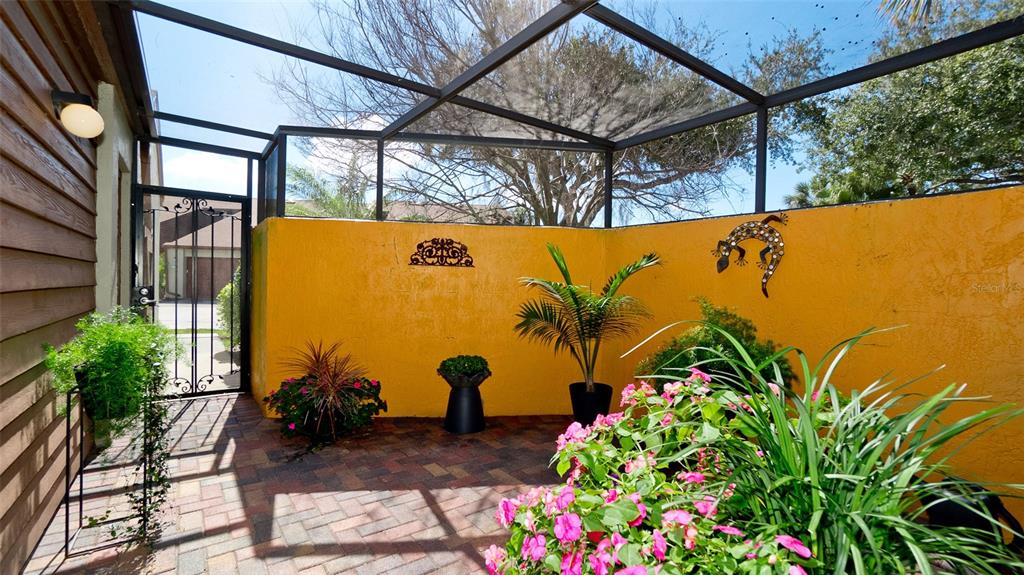 A screened-in patio features yellow walls, a brick floor, and several potted plants — 4527 PARK LAKE TERRACE N, BRADENTON, FL