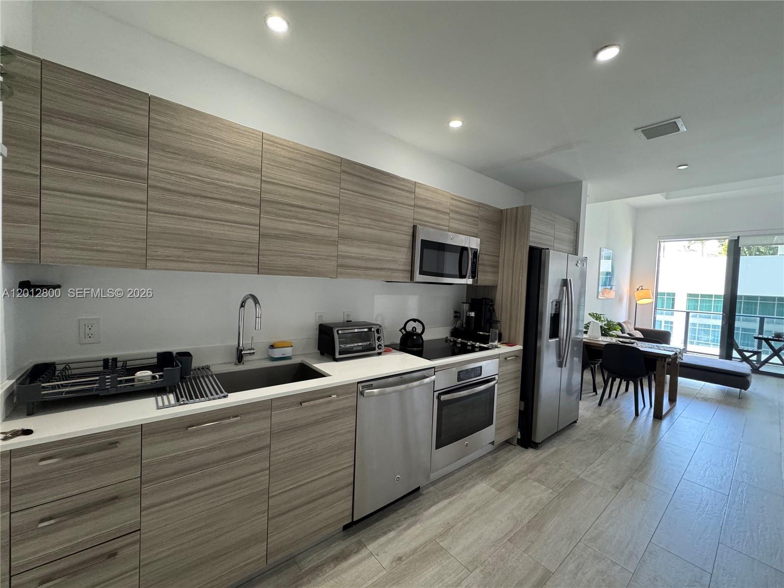 A modern kitchen features wood-grain cabinetry, stainless steel appliances, and light-colored tile flooring — 121 NE 34th St # L601, Miami FL 33137, MIAMI, FL