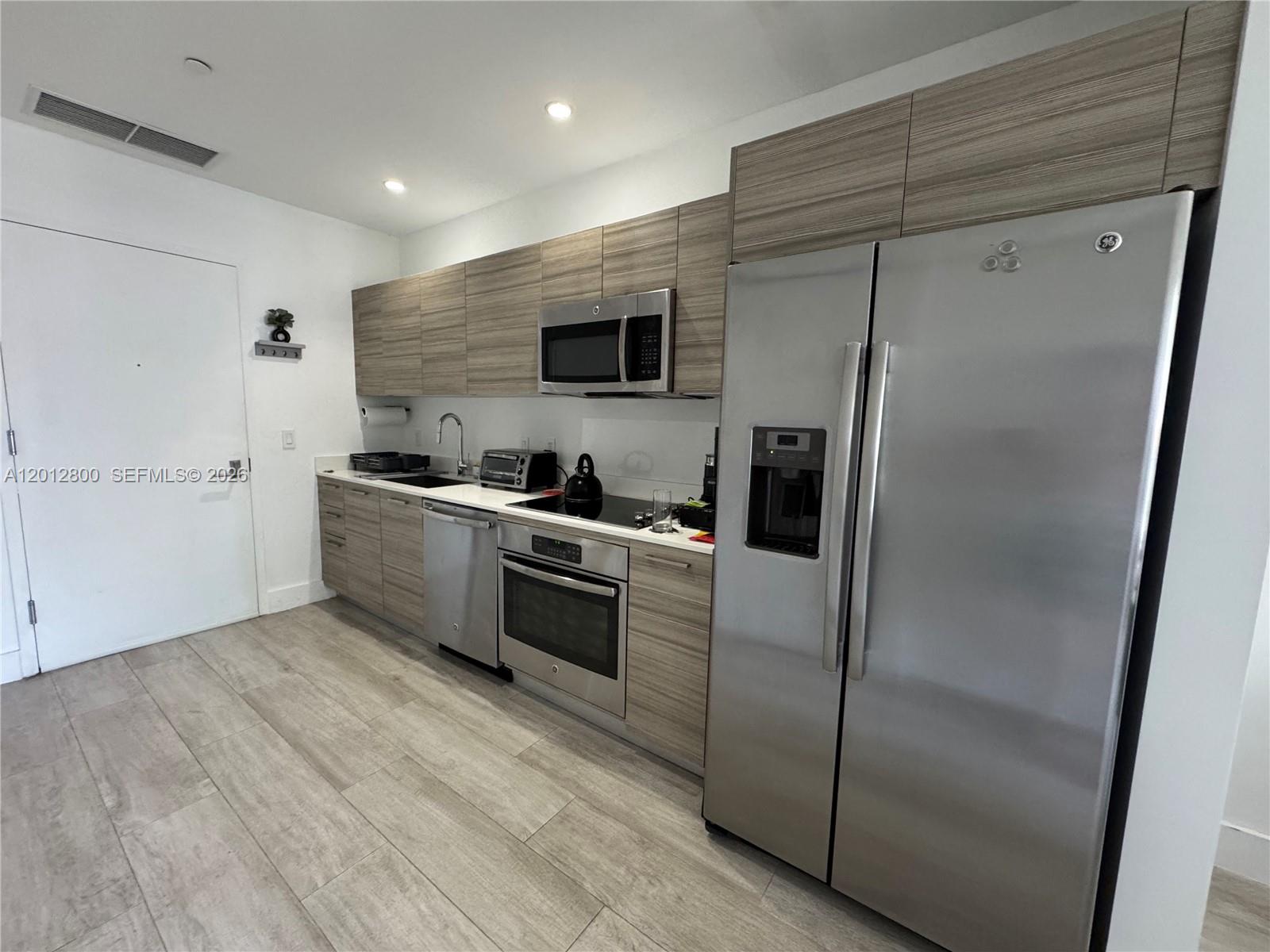 A living room with a grey sectional sofa, wooden media console, and an adjacent dining area — 121 NE 34th St # L601, Miami FL 33137, MIAMI, FL