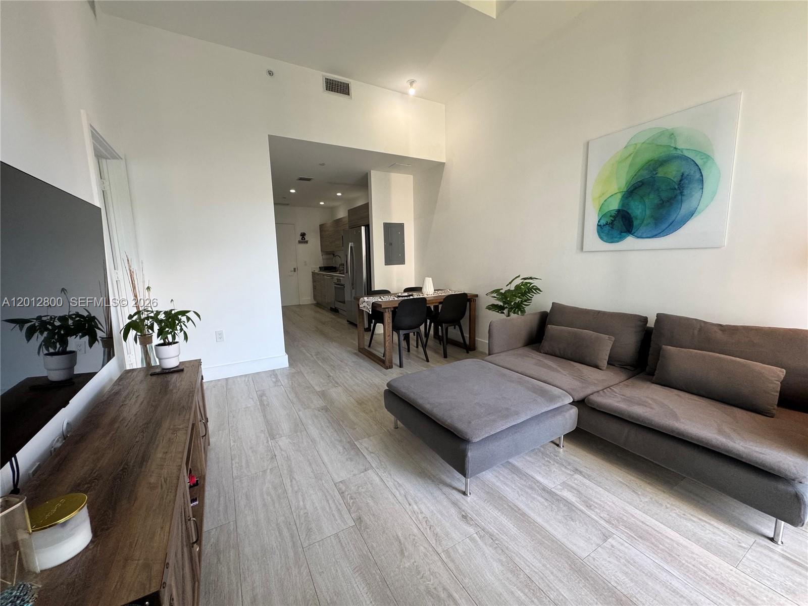 A living room features a grey sectional sofa, a wooden media console, and dining area — 121 NE 34th St # L601, Miami FL 33137, MIAMI, FL