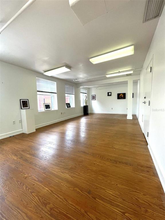 An empty room with hardwood floors, white walls, large windows, and overhead fluorescent lighting — 1624-1630 E 7TH AVENUE, TAMPA, FL