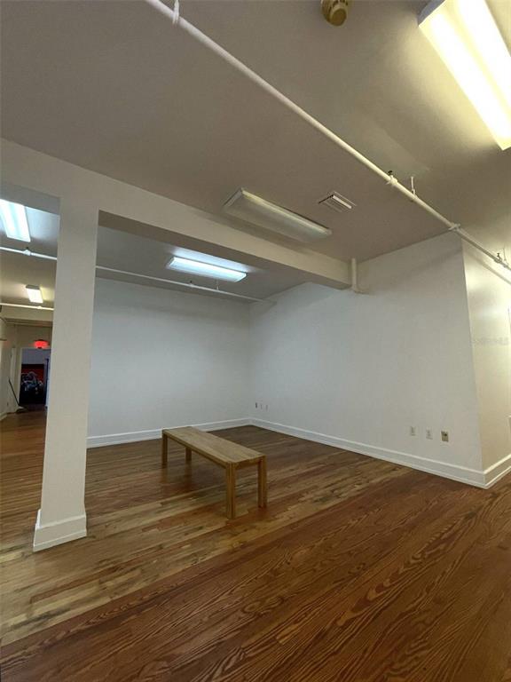 An empty room features hardwood floors, white walls, a wooden bench, and overhead fluorescent lighting — 1624-1630 E 7TH AVENUE, TAMPA, FL