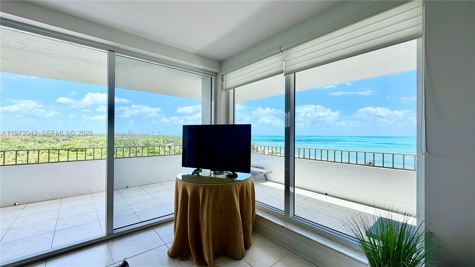 A television sits on a round table in a room with floor-to-ceiling windows overlooking the ocean — 177 Ocean Lane Dr # 1008, Key Biscayne FL 33149, KEY BISCAYNE, FL