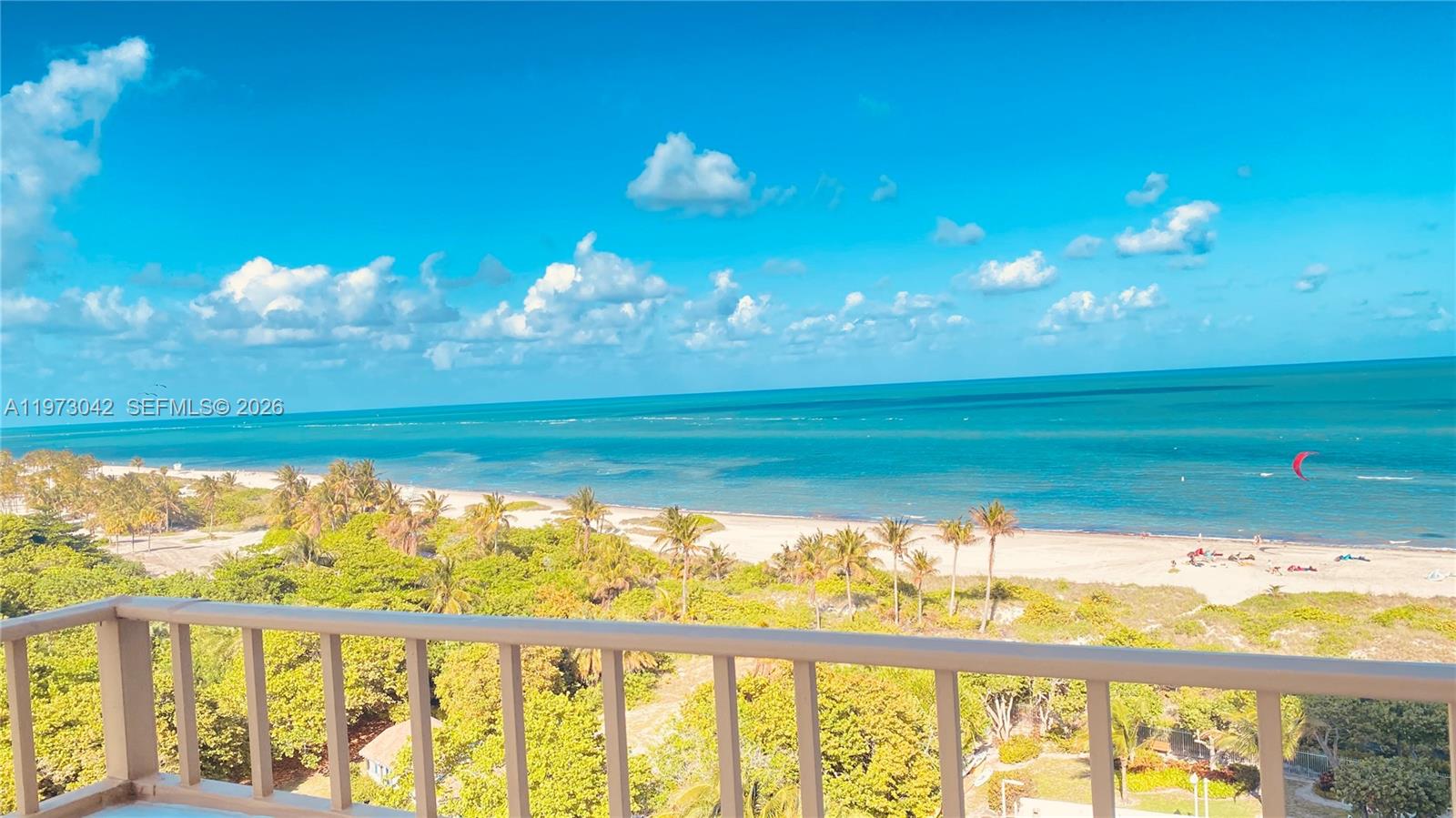 A balcony overlooks a sandy beach, lush green trees, and the ocean under a blue sky — 177 Ocean Lane Dr # 1008, Key Biscayne FL 33149, KEY BISCAYNE, FL