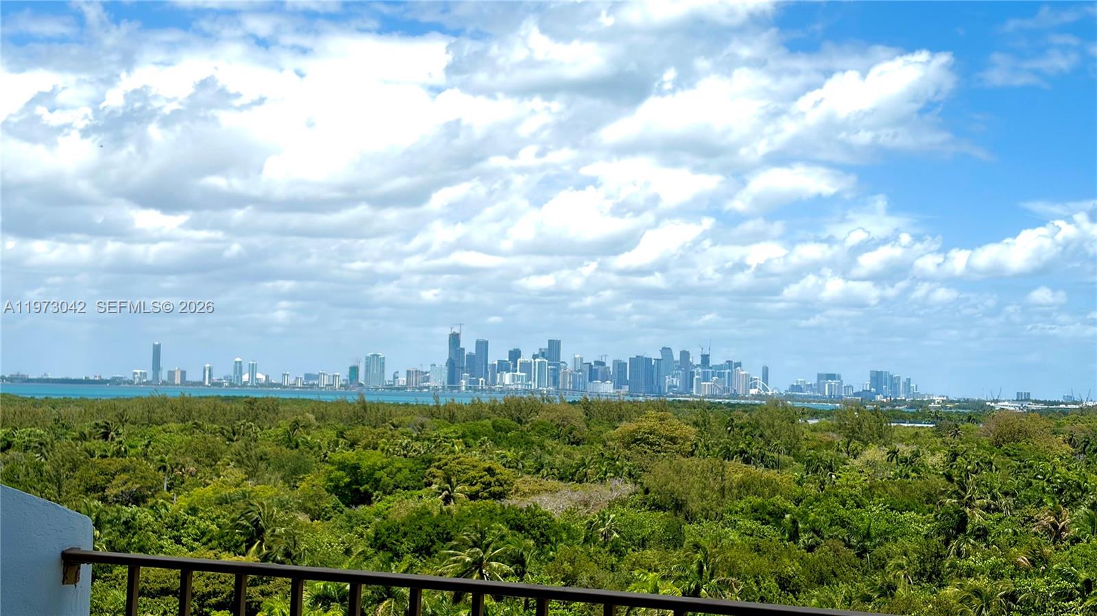 A balcony overlooks a dense forest with a distant city skyline across the water — 177 Ocean Lane Dr # 1008, Key Biscayne FL 33149, KEY BISCAYNE, FL