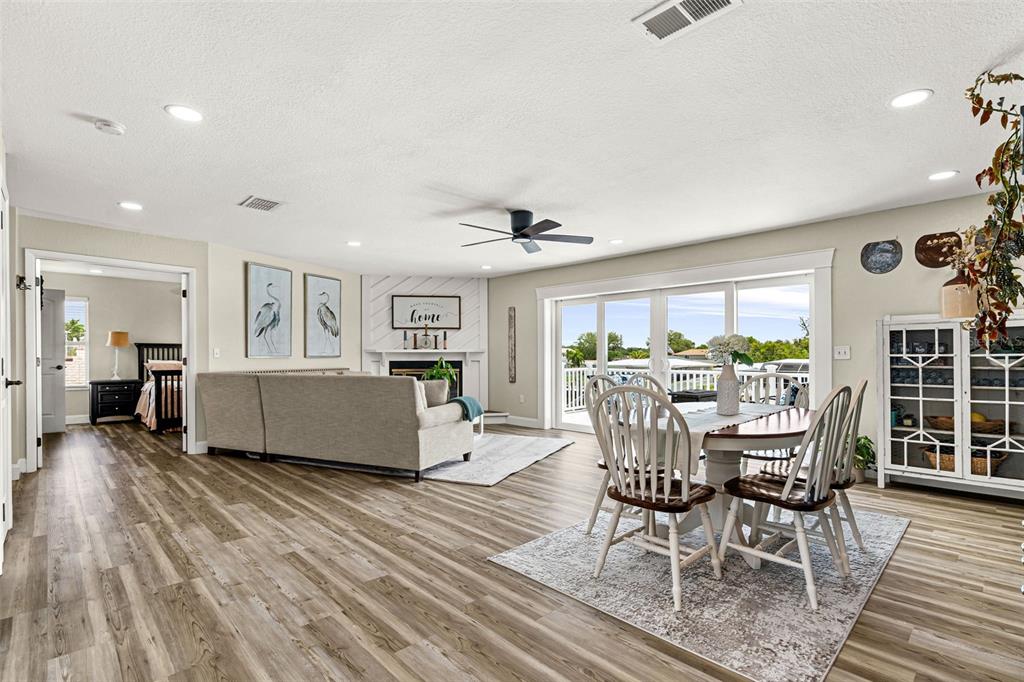 An open-concept living and dining area features wood-look flooring, a fireplace, and sliding glass doors — 5404 BAY STATE ROAD, PALMETTO, FL