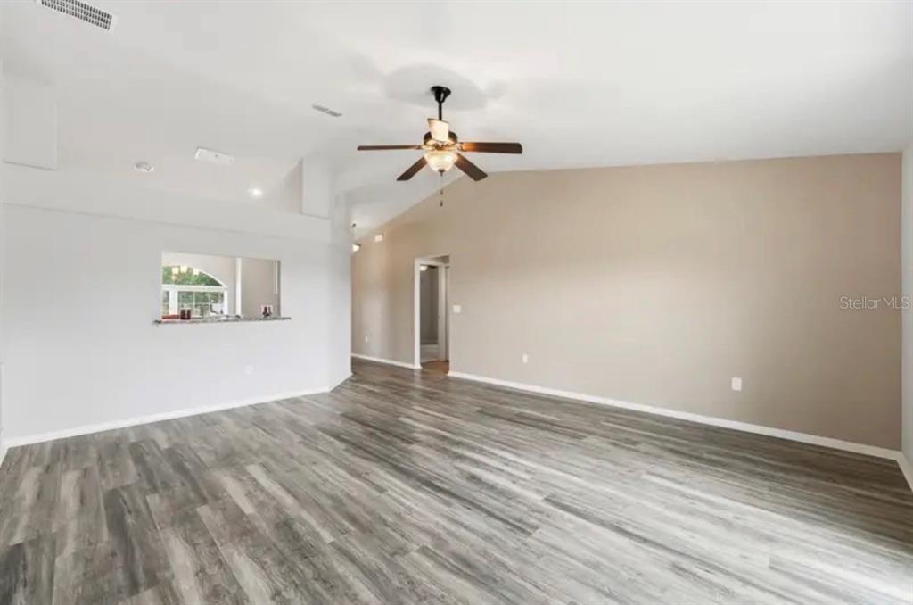 An empty living room features wood-look flooring, a vaulted ceiling, and a ceiling fan — 202 HIGHLAND MEADOWS PLACE, DAVENPORT, FL