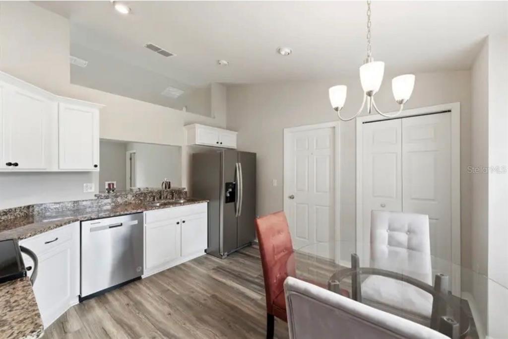 A kitchen with white cabinets, granite countertops, stainless steel appliances, and an adjacent dining area — 202 HIGHLAND MEADOWS PLACE, DAVENPORT, FL
