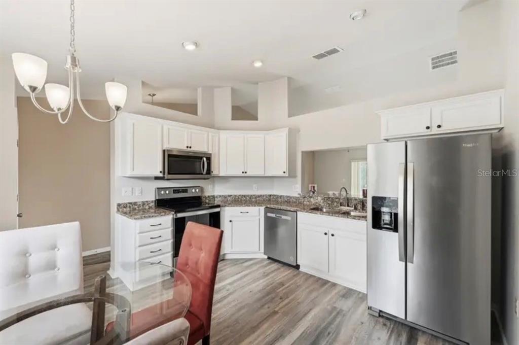 A kitchen with white cabinets, granite countertops, stainless steel appliances, and wood-look flooring — 202 HIGHLAND MEADOWS PLACE, DAVENPORT, FL