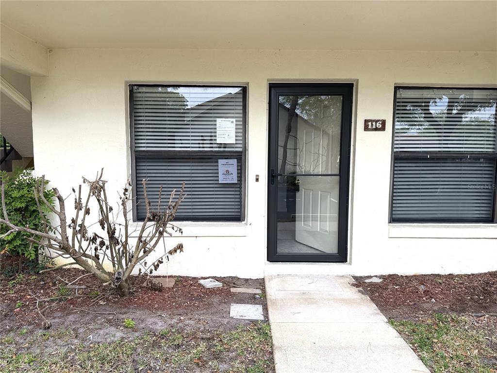 The exterior view shows a ground-level apartment entrance with a screen door and two windows — 112 LACOSTA LANE UNIT 116, DAYTONA BEACH, FL
