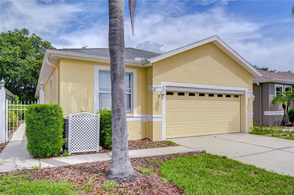 A yellow single-story house features a two-car garage, a white lattice fence, and a palm tree — 8049 SANGUINELLI ROAD, LAND O LAKES, FL