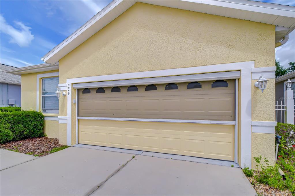 A yellow house exterior features a two-car garage with a retractable screen door — 8049 SANGUINELLI ROAD, LAND O LAKES, FL