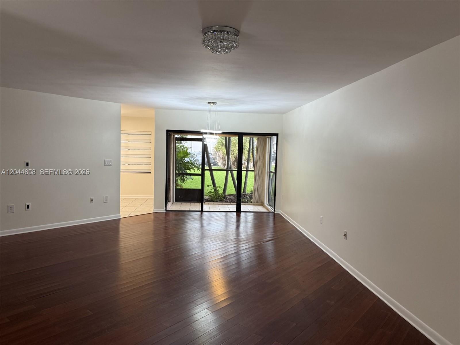 An empty living room features dark hardwood floors, white walls, and a sliding glass door — 9686 SW 138th Ave # 9686, Miami FL 33186, MIAMI, FL