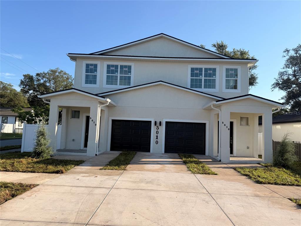 A two-story duplex with a light-colored exterior, two dark garage doors, and covered entryways — 5010 E 32ND AVENUE UNIT 2, TAMPA, FL
