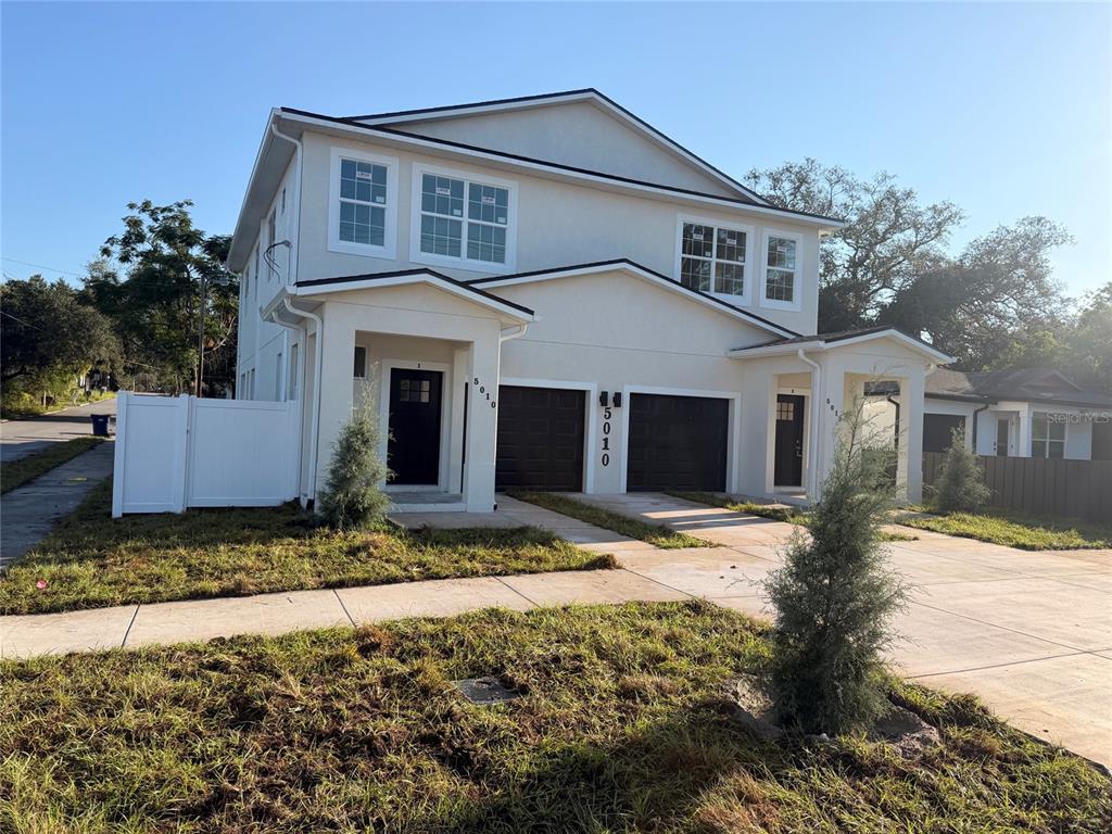 A two-story duplex with white stucco siding, two dark garages, and a concrete driveway — 5010 E 32ND AVENUE UNIT 2, TAMPA, FL