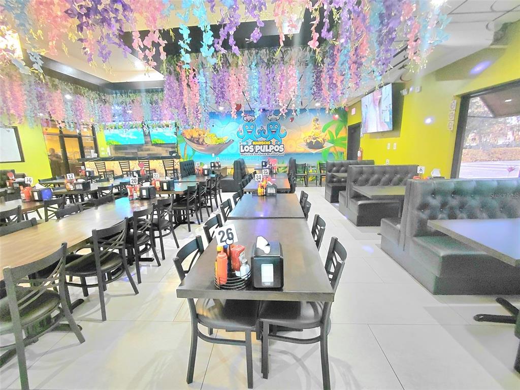 A restaurant interior features rows of tables, black booths, and hanging floral decorations — 909 W VINE STREET, KISSIMMEE, FL