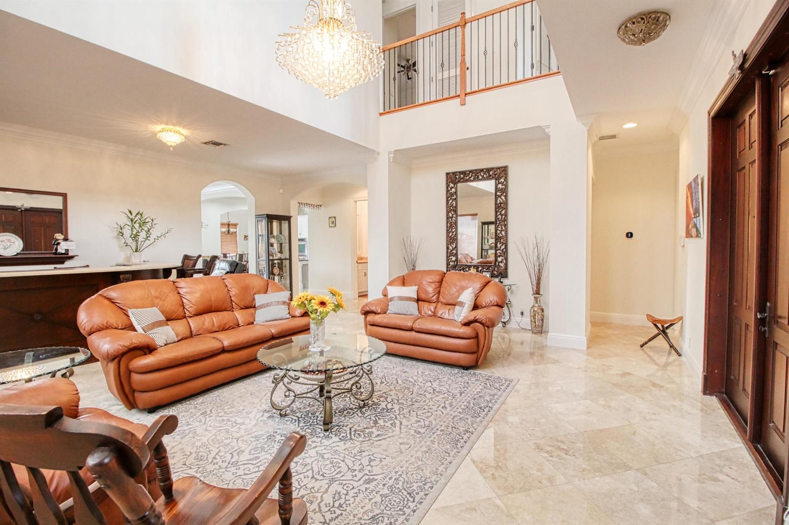 A spacious living room features leather sofas, a glass coffee table, and a grand chandelier — 8192 Canopy Terrace, Parkland FL 33076, PARKLAND, FL