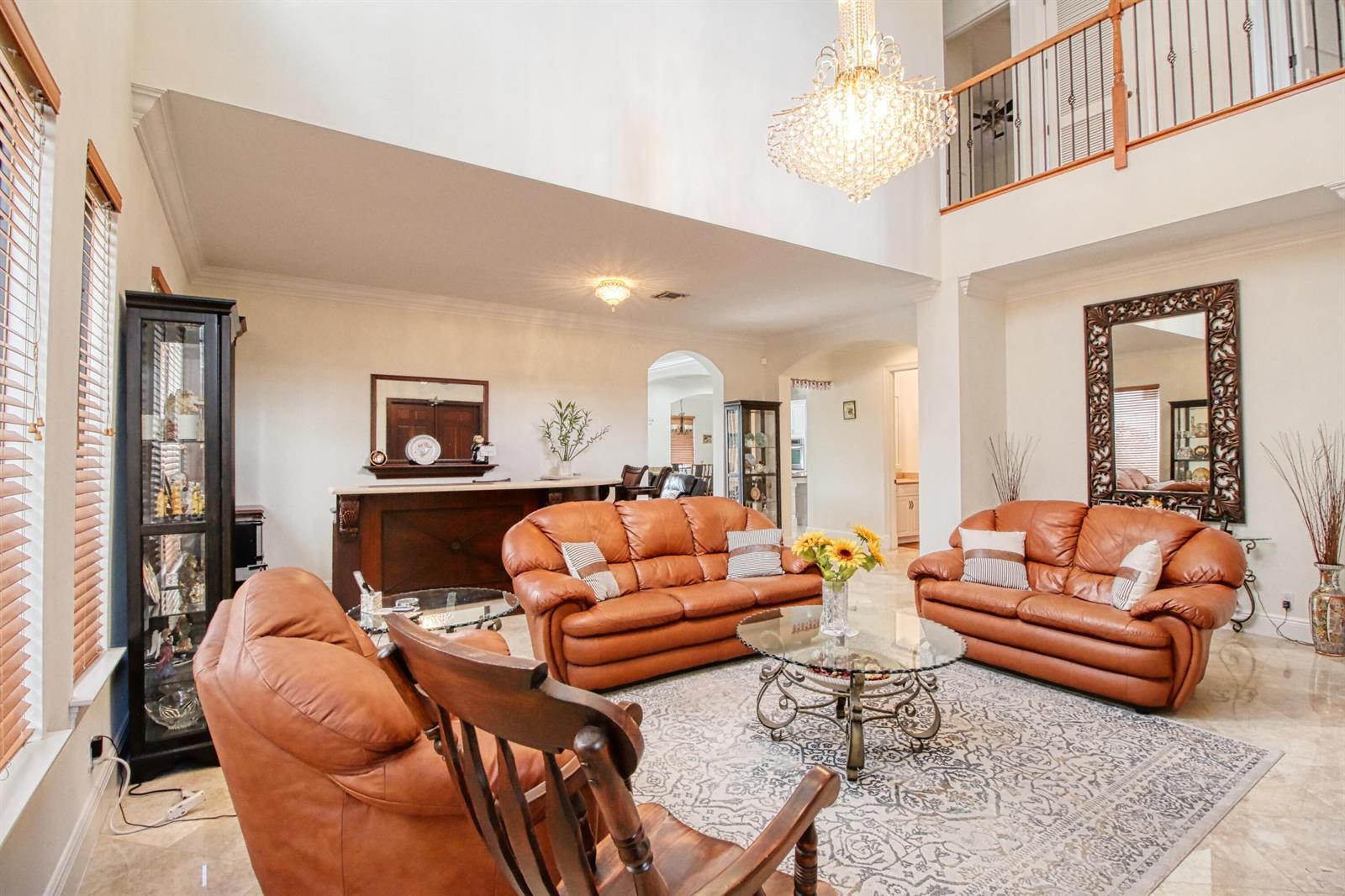 A spacious living room features leather sofas, a glass coffee table, and a crystal chandelier — 8192 Canopy Terrace, Parkland FL 33076, PARKLAND, FL