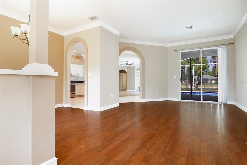 A living area with hardwood floors, arched doorways, and sliding glass doors leading to a pool — 2456 APPALOOSA TRAIL, PALM HARBOR, FL