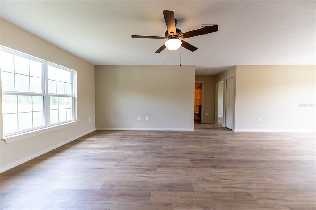 An empty room features wood-look flooring, beige walls, a ceiling fan, and a large window — 5911 NW 63RD PLACE, OCALA, FL