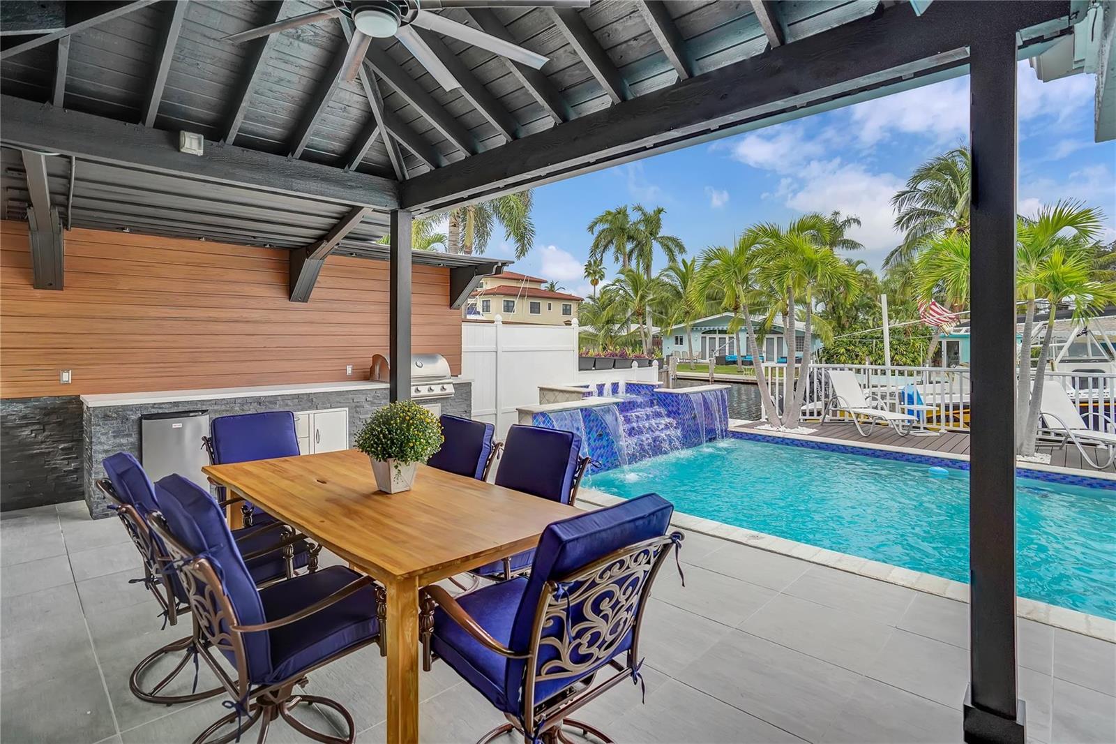 A covered patio features a dining set, outdoor kitchen, and a pool with a waterfall — 2363 SE 15th Street, Pompano Beach FL 33062, POMPANO BEACH, FL