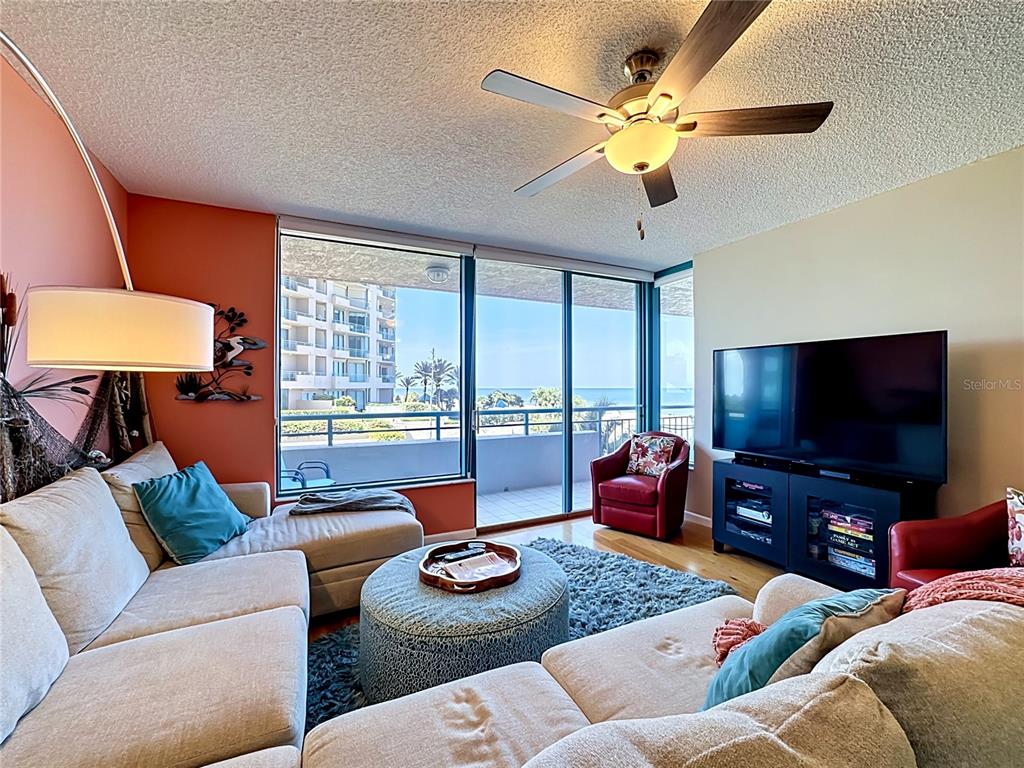 A living room features a sectional sofa, a television, and a balcony with ocean views — 1540 GULF BOULEVARD UNIT 304, CLEARWATER BEACH, FL
