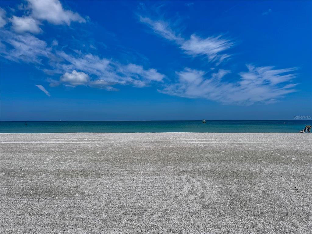 A wide, sandy beach meets the calm ocean under a bright blue sky — 1540 GULF BOULEVARD UNIT 304, CLEARWATER BEACH, FL