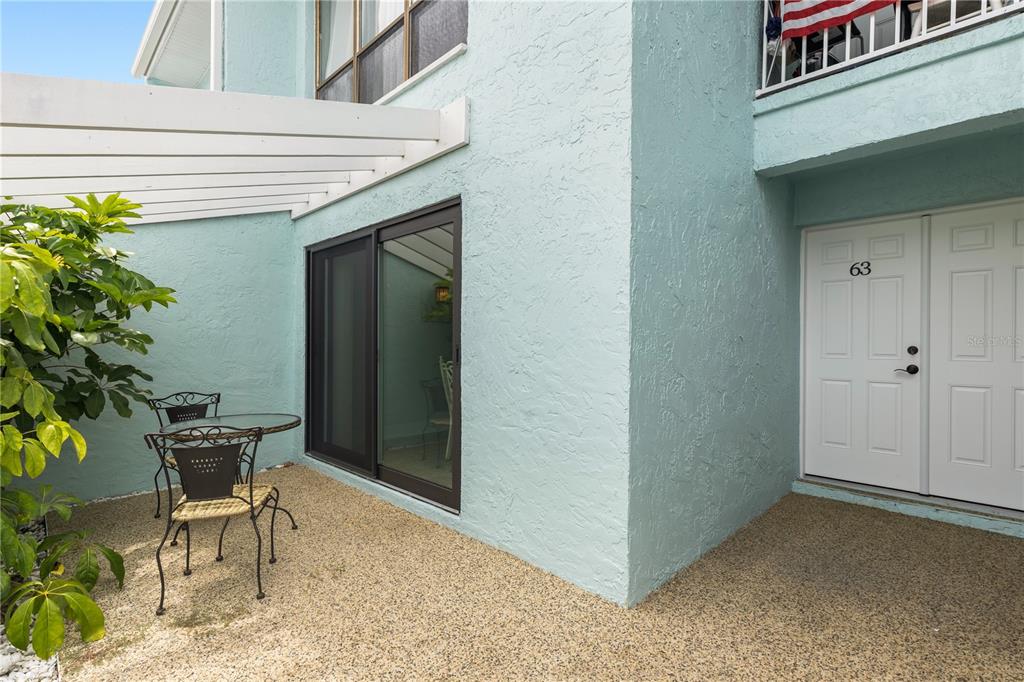 A patio with a small table and chairs sits beside a sliding glass door — 1 WINDRUSH BOULEVARD UNIT 63, INDIAN ROCKS BEACH, FL