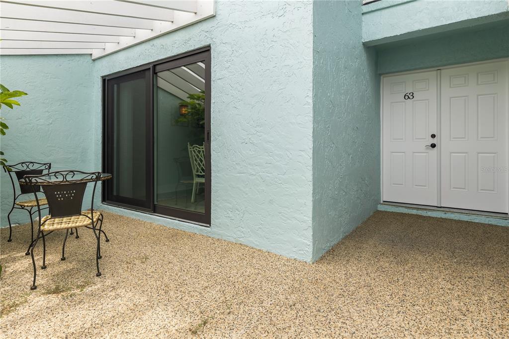 A patio with a table and chairs sits beside a light blue building entrance — 1 WINDRUSH BOULEVARD UNIT 63, INDIAN ROCKS BEACH, FL