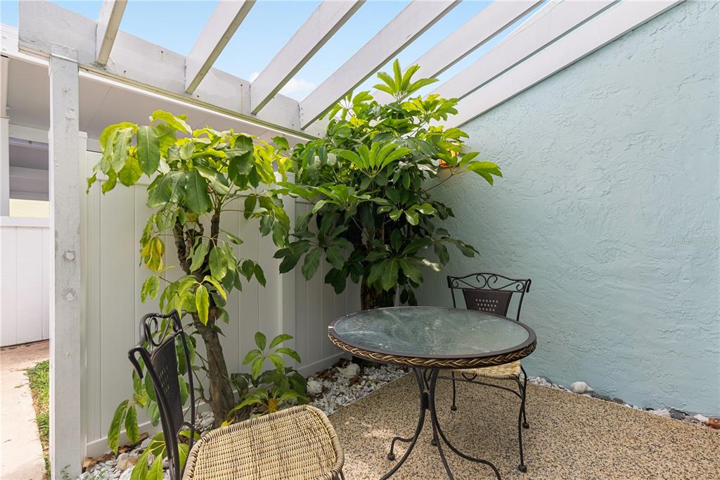 A small outdoor patio features a glass-topped table, two chairs, and potted plants — 1 WINDRUSH BOULEVARD UNIT 63, INDIAN ROCKS BEACH, FL