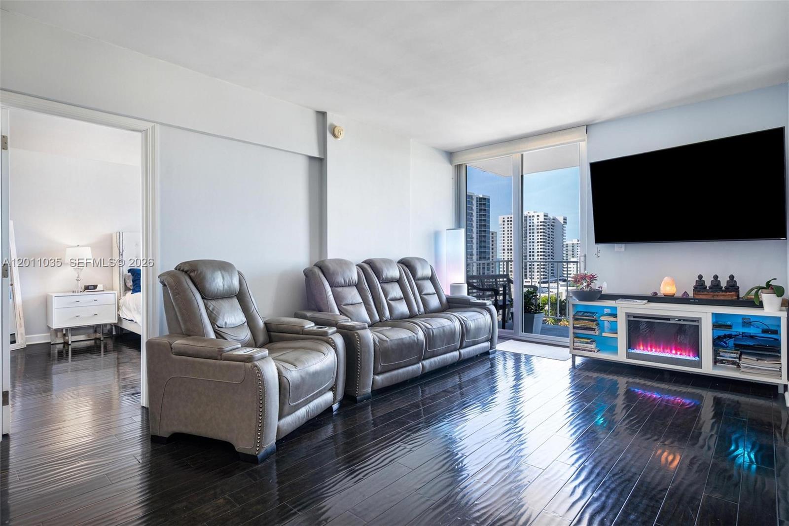 A living room features dark hardwood floors, gray leather seating, and a wall-mounted television — 2829 Indian Creek Dr # 1209, Miami Beach FL 33140, MIAMI BEACH, FL