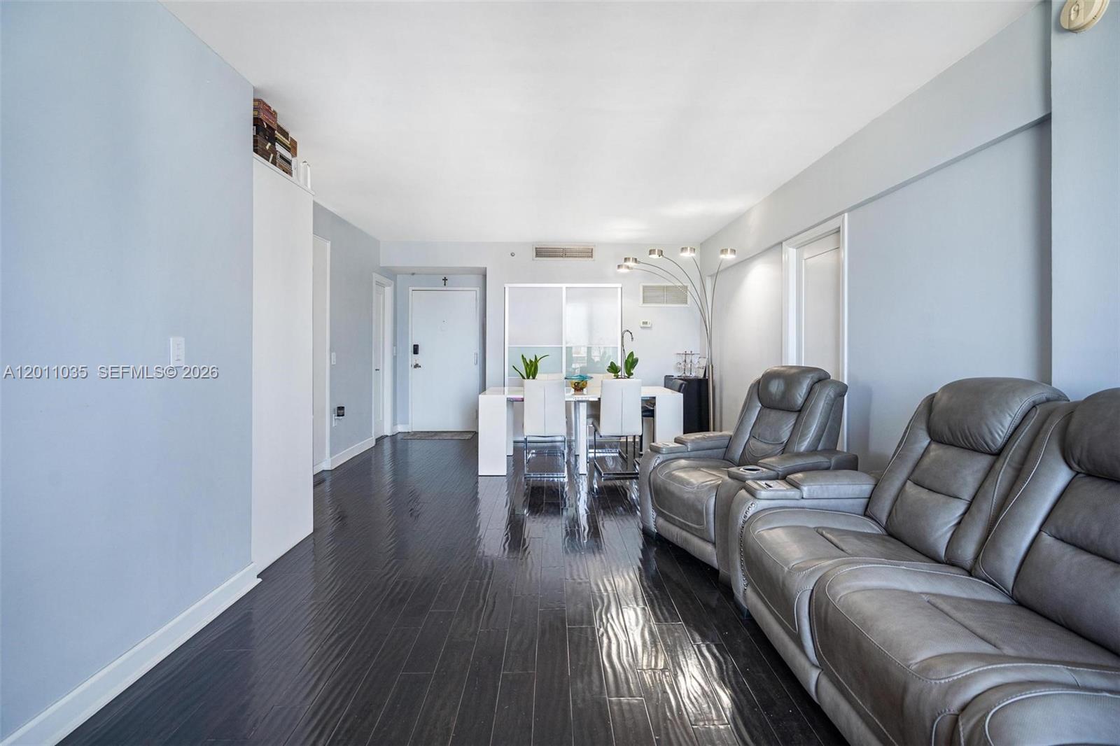 A living and dining area features dark wood floors, light blue walls, and gray recliners — 2829 Indian Creek Dr # 1209, Miami Beach FL 33140, MIAMI BEACH, FL