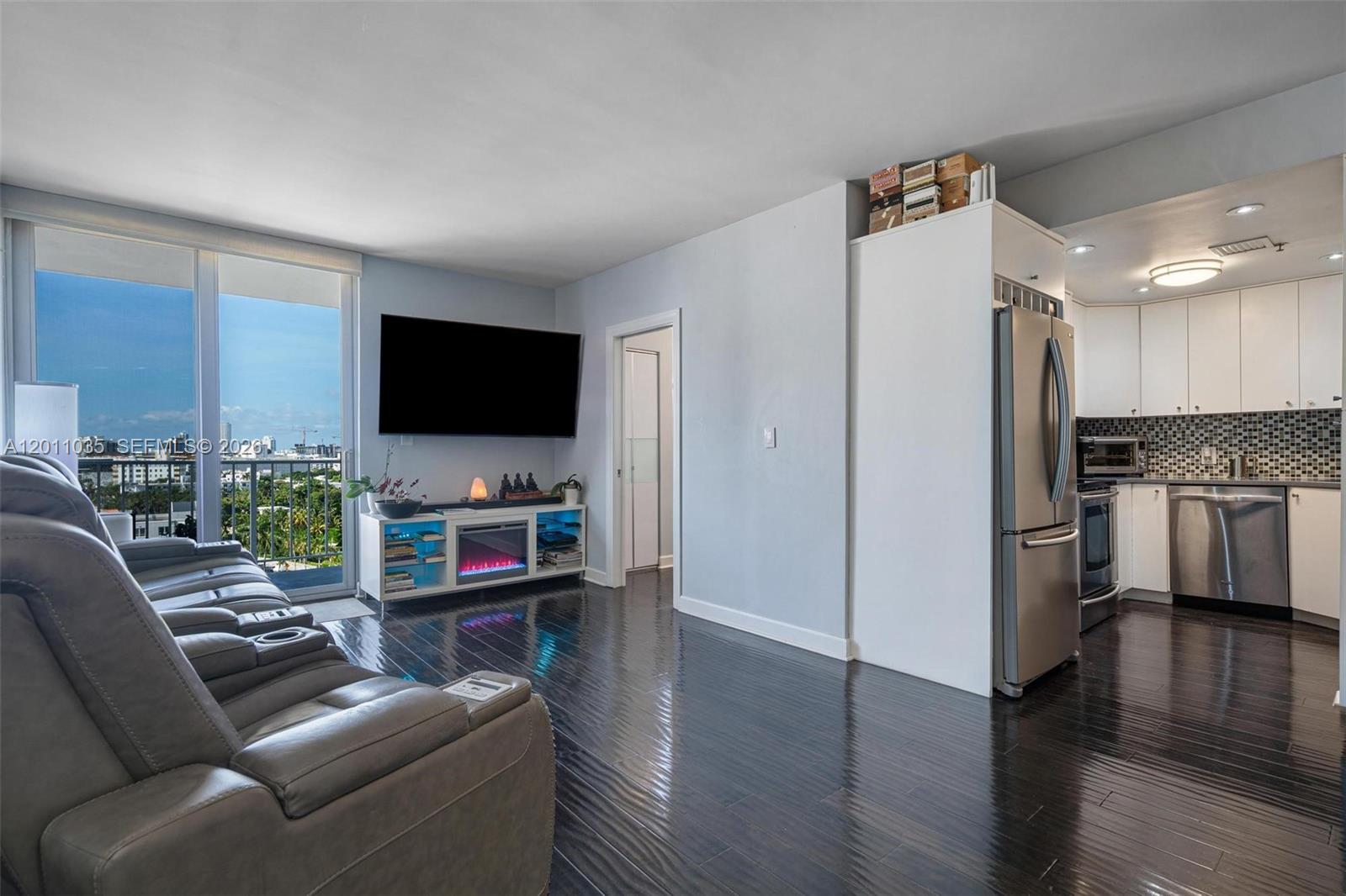 A living room with dark wood floors, a fireplace console, and an adjacent kitchen — 2829 Indian Creek Dr # 1209, Miami Beach FL 33140, MIAMI BEACH, FL