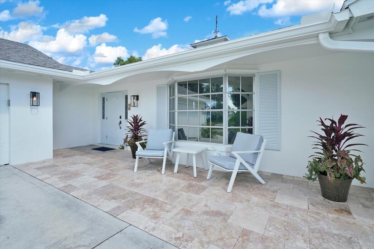 A white house exterior features a stone patio with two chairs and potted plants — 76 W Fairview W, Tequesta FL 33469, TEQUESTA, FL
