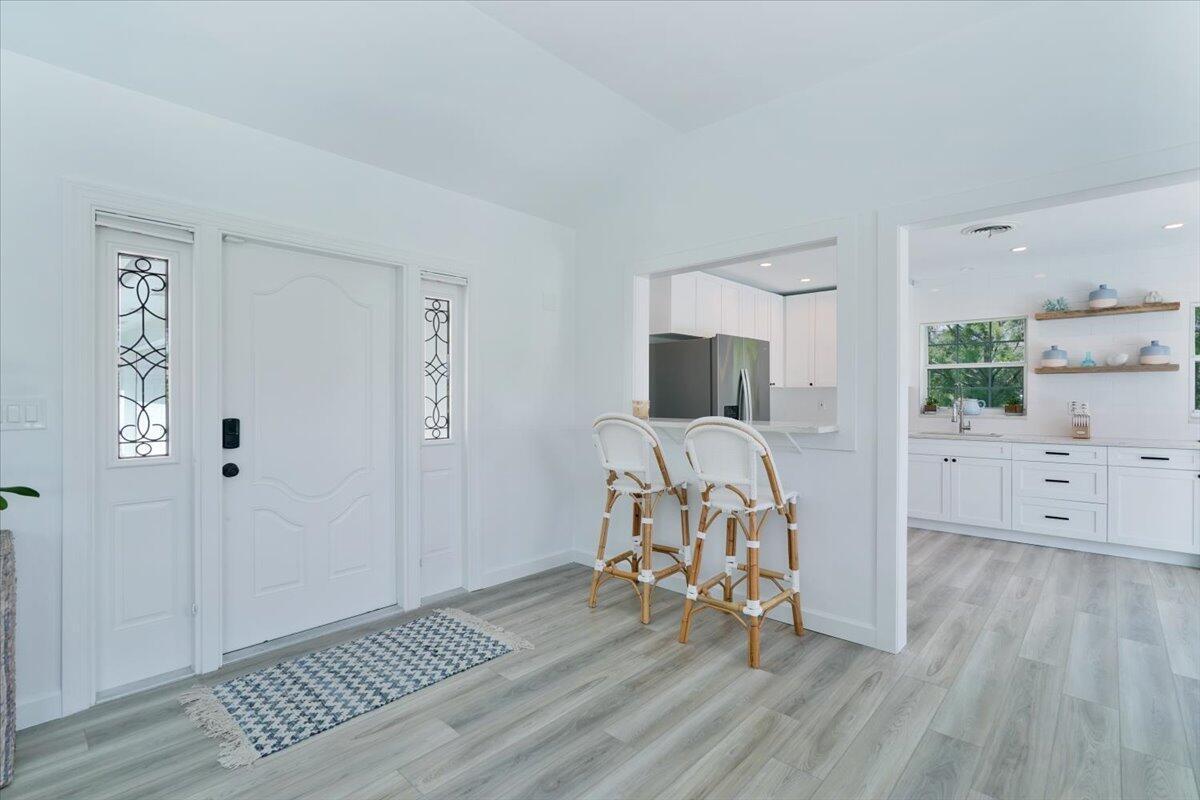 An entryway with a white front door leads into a kitchen featuring a breakfast bar — 76 W Fairview W, Tequesta FL 33469, TEQUESTA, FL