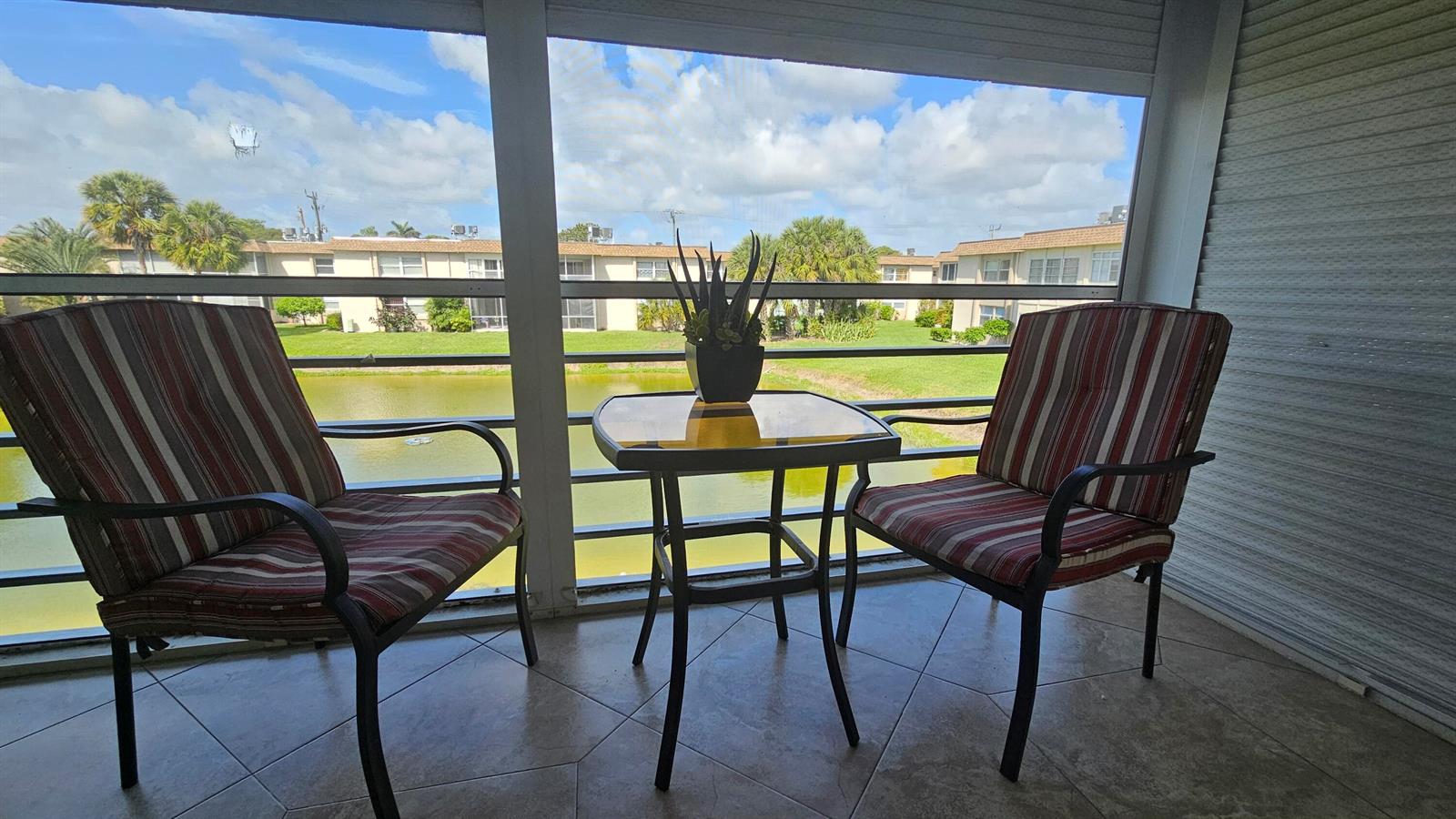 A screened-in patio features two striped chairs, a small table, and a view of water — 504 Davis Road # 96, Palm Springs FL 33461, PALM SPRINGS, FL