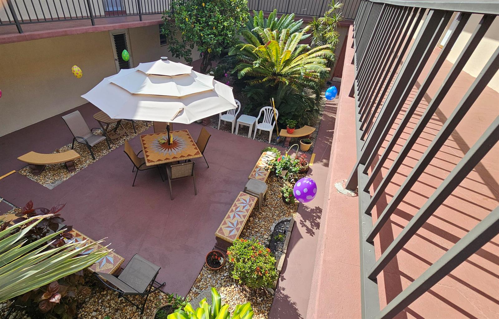 An elevated view of a courtyard patio featuring a dining set, umbrella, and potted plants — 504 Davis Road # 96, Palm Springs FL 33461, PALM SPRINGS, FL