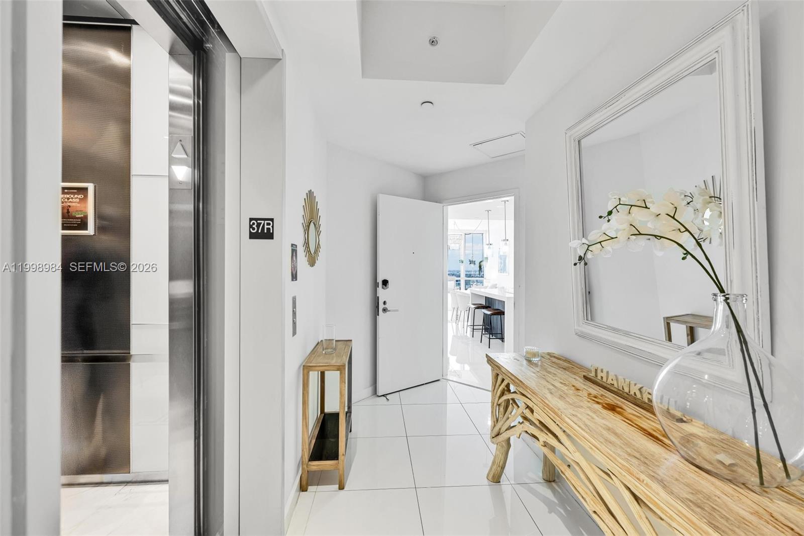A white-tiled entryway features a wooden console table, a large mirror, and an open door — 851 NE 1st Ave # 3708, Miami FL 33132, MIAMI, FL